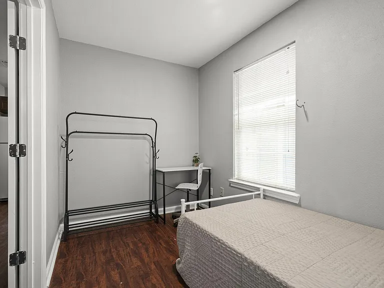 Twin sized bed & mattress in a cozy bedroom w/ writing desk & chair, closet rack.