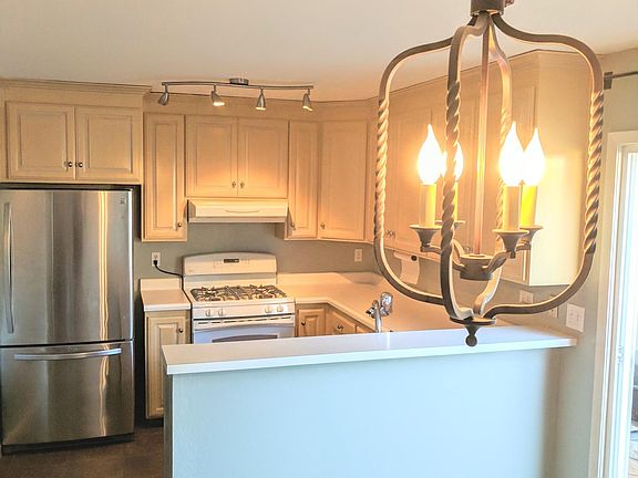 Bright kitchen with stainless appliances, a white stove, and generous cabinets. The breakfast bar opens to the living space, with sliding doors to the patio and a carpeted staircase leading upstairs.