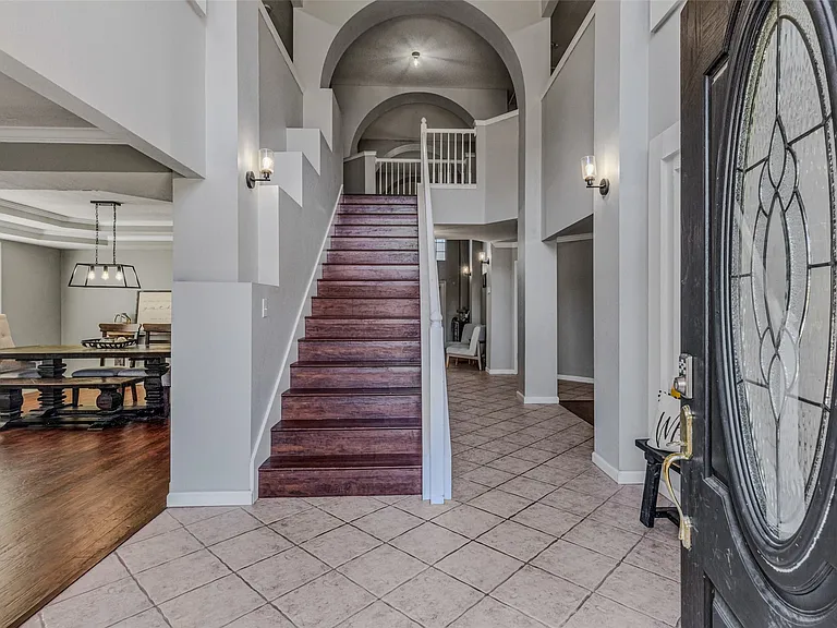 Foyer featuring a grand staircase with dark wood treads and white risers, arched doorways, tile flooring, and sconce lighting