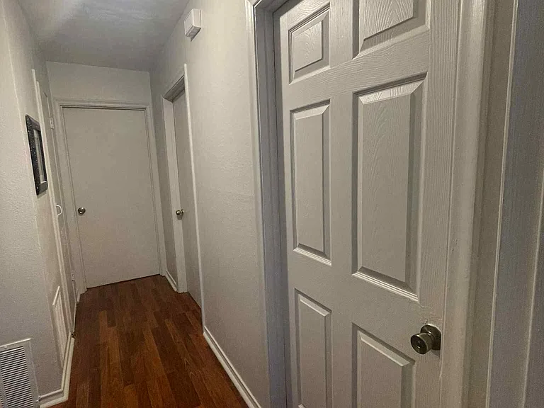Hallway view showing the easy flow between the bedrooms and bathroom, featuring consistent wood flooring throughout the living areas.