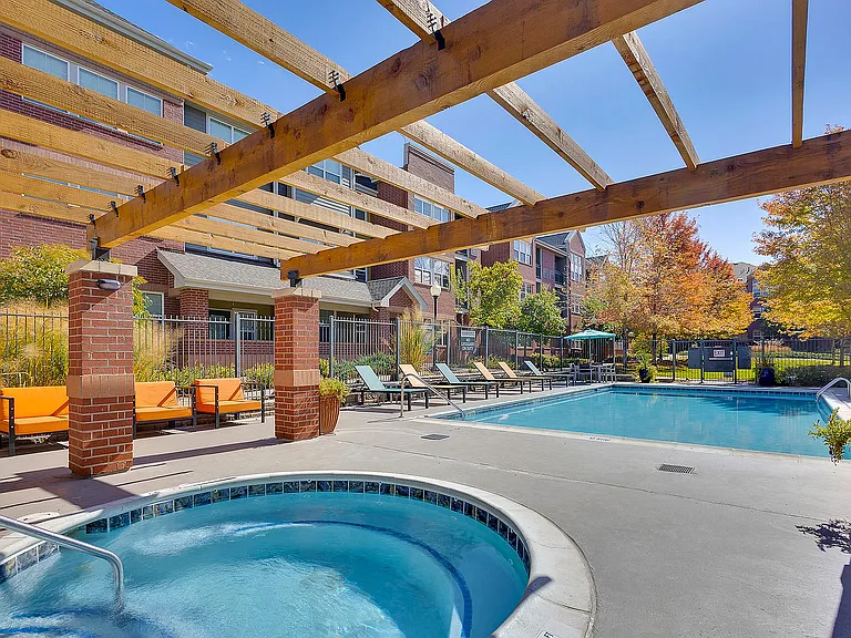 Inviting outdoor pool area with a relaxing hot tub and stylish pergola, surrounded by comfortable lounge chairs and vibrant autumn foliage.