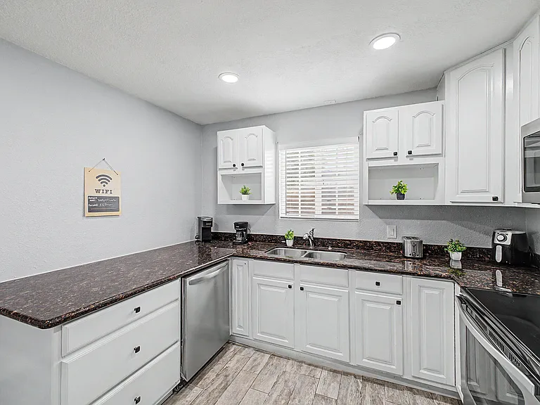 U-shaped kitchen with ample counter space, white cabinetry, double-basin sink, and stainless appliances for easy cooking.