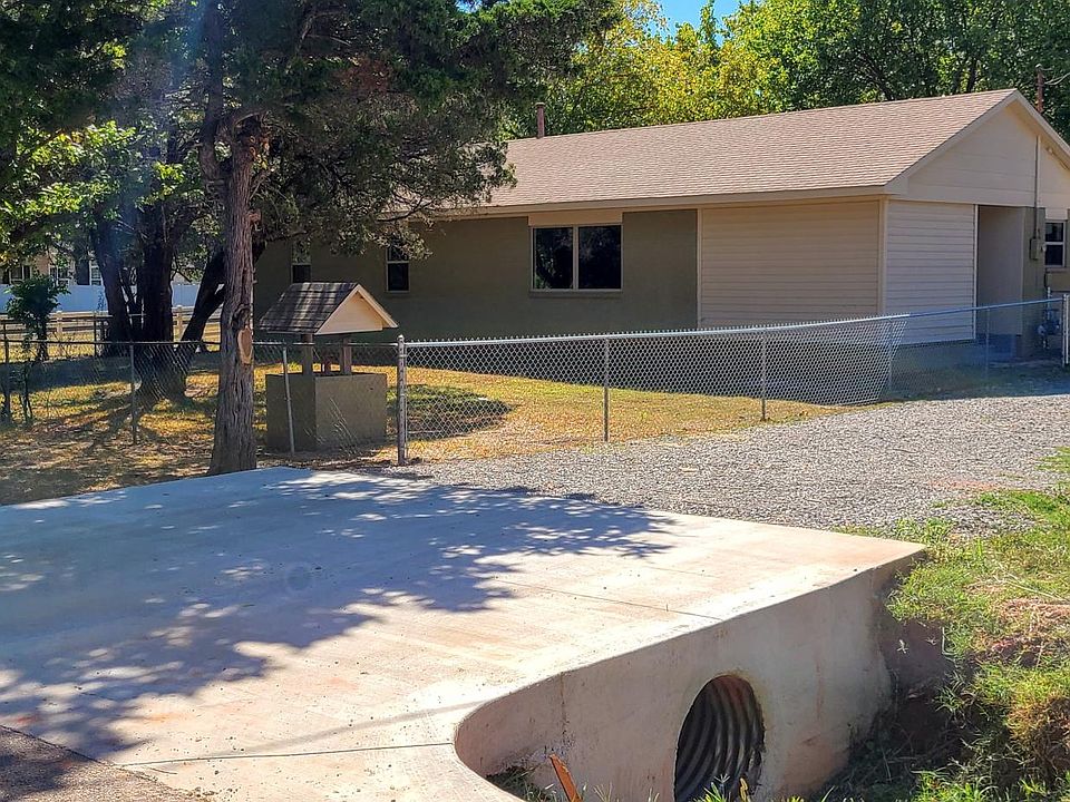Street view. Fully fenced front yard with large gate opening to allow for a riding lawn mower. 2-car carport