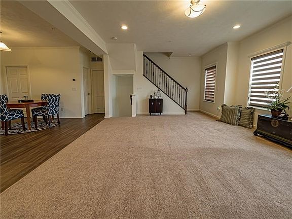 The expansive family room features custom blinds, crown molding, neutral carpet and a wrought iron staircase leading to the seco