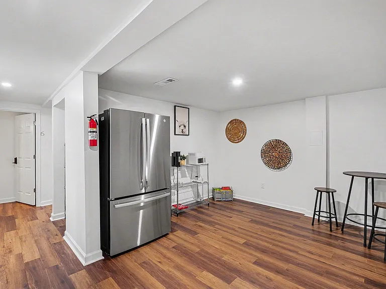 Open common area with wood-look flooring, full-size refrigerator, and a cafe-height table for quick meals or work.