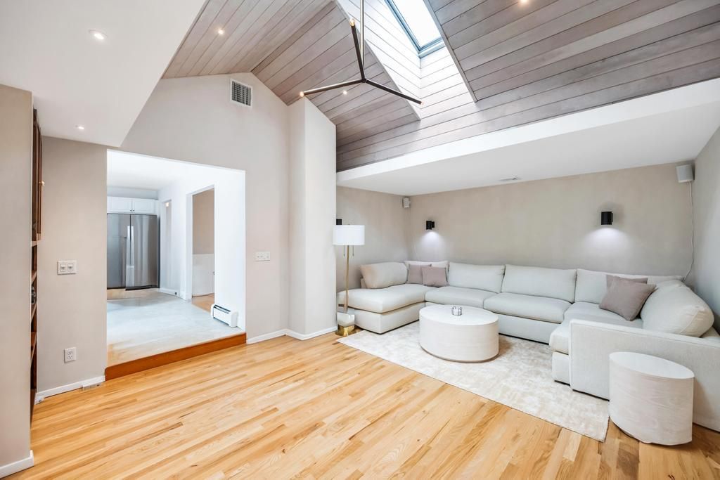 Spacious Living room with high ceilings, skylights, large couch, tv, and fireplace.