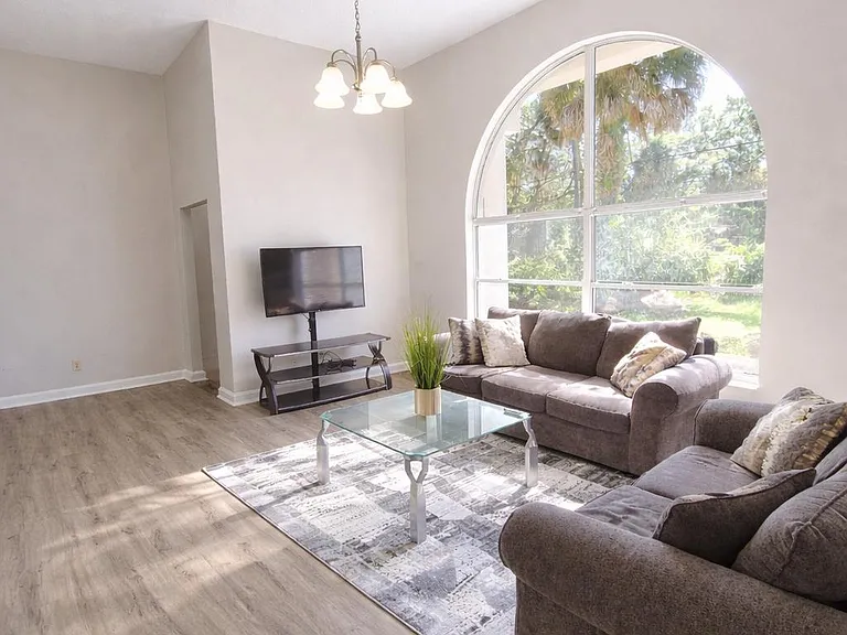 Spacious living room with high ceilings, large arched window, and a comfortable seating layout for relaxing or hosting.