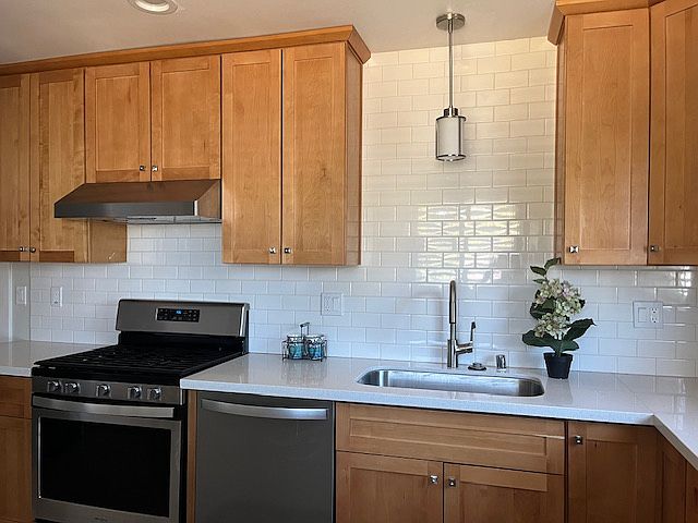 Beautifully remodeled eat-in kitchen has natural maple wood cabinets, stainless steel appliances, white quartz counter top and white subway tile back splash, gray tile floors.