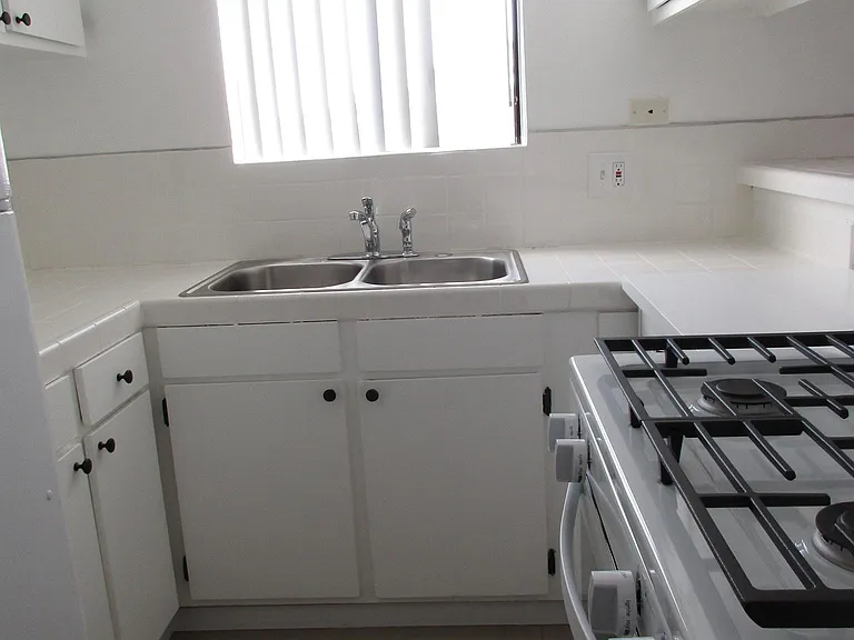 KITCHEN WITH UPPER AND LOWER CABINETRY, RANGE, REFRIGERATOR, AND A WINDOW ABOVE THE SINK FOR LIGHT AND AIR.