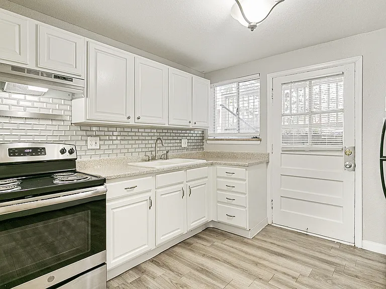 Bright and modern kitchen with sleek stainless steel oven, white shaker cabinets, stylish backsplash, and natural light from large windows.