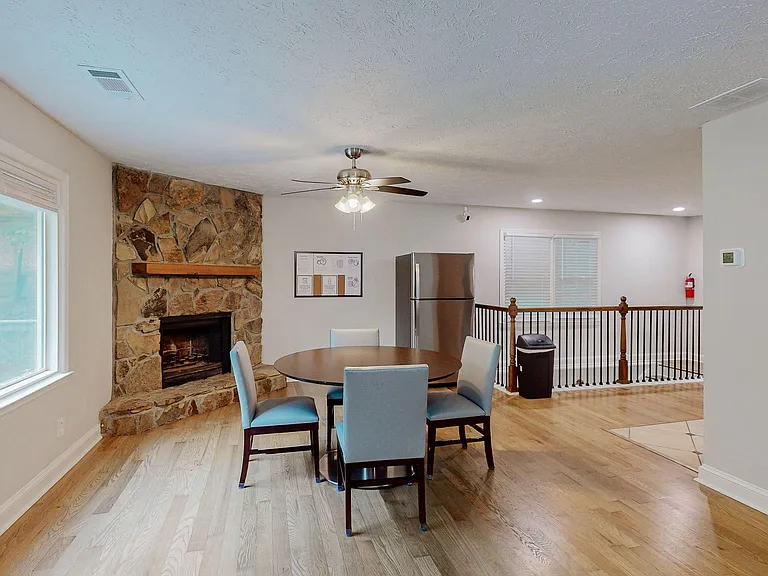 Open dining area with a round table, hardwood floors, and a stone fireplace, plus nearby windows for natural light.