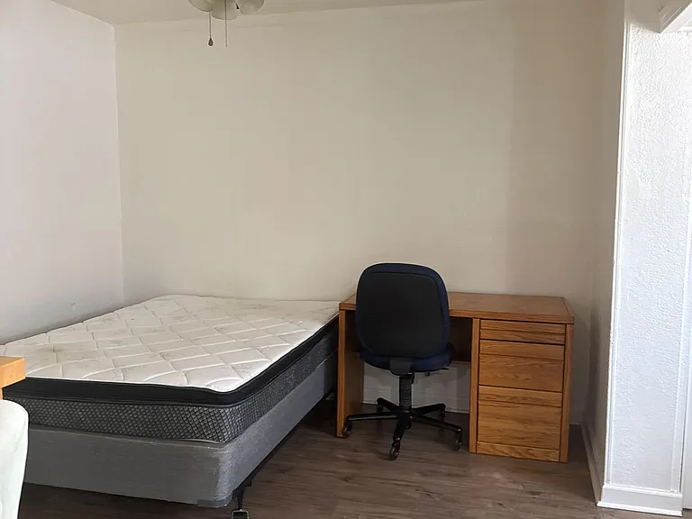 Furnished bedroom with bed, work desk and chair, ceiling fan, and durable wood-look flooring for easy upkeep.