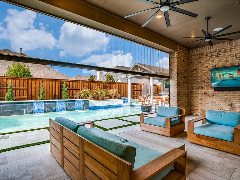 Covered outdoor living space featuring brick wall, ceiling fans, and a wall-mounted display
