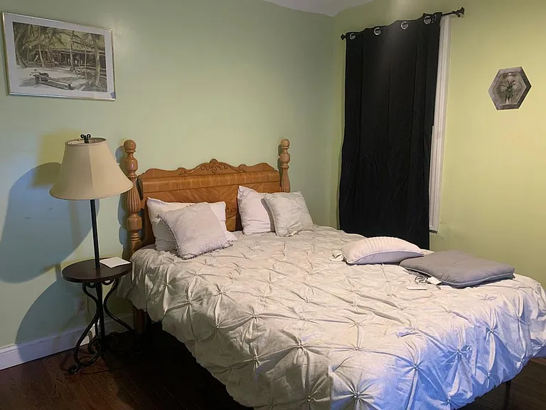 Furnished bedroom with a full-size bed, bedside table and lamp, and a window with blackout curtains for added privacy.
