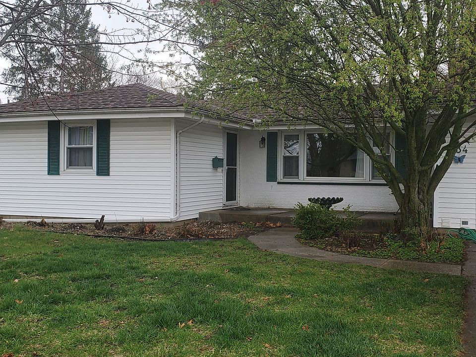 Front view of home, small flower bed, and one step up to a cement porch, large enough for a couple chairs or swing.