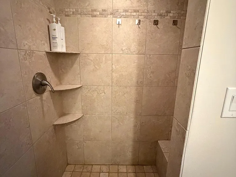 Walk-in tiled shower with corner shelving, built-in bench, and multiple wall hooks for convenient storage and comfort.