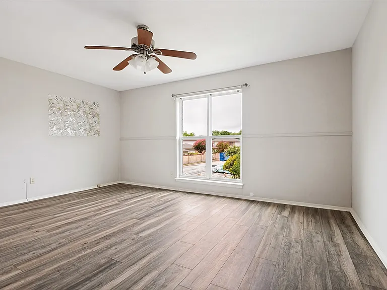 Spacious room featuring wood-finish flooring, a large window, a ceiling fan with integrated lighting, and neutral wall tones