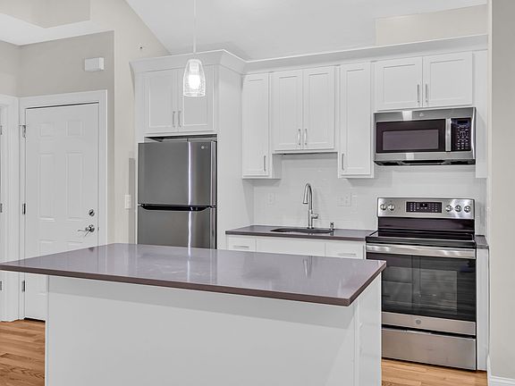 Kitchen with stainless steel refrigerator, electric range and microwave with view of 2nd entry door.