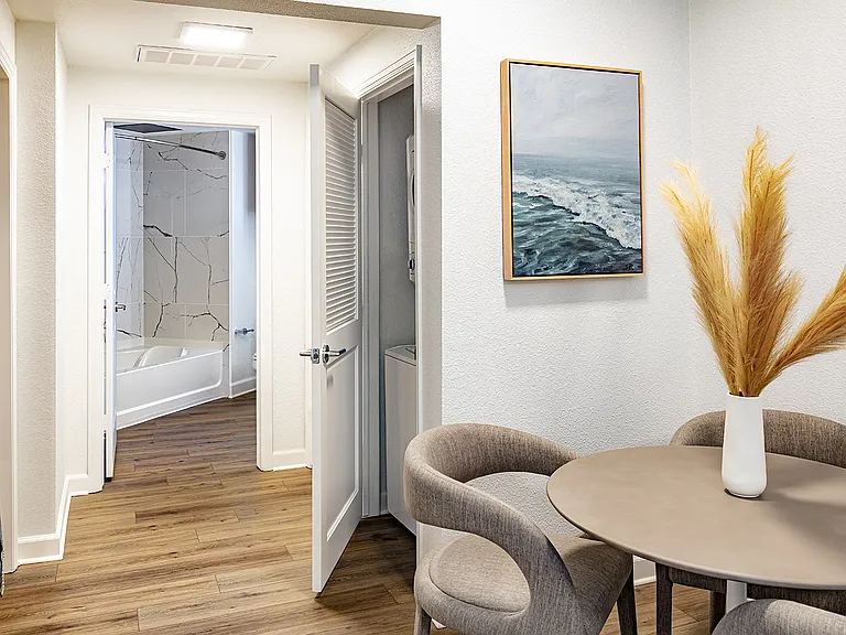 A hallway with a dining table, a laundry closet, and a view into the tiled bathroom.