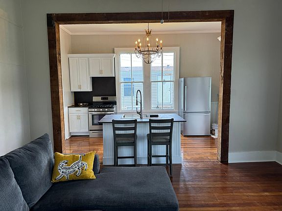 View from living room to new island, new fridge, new cabinets with classic brass pulls and amazing chandelier, beautiful tall windows and high ceilings..