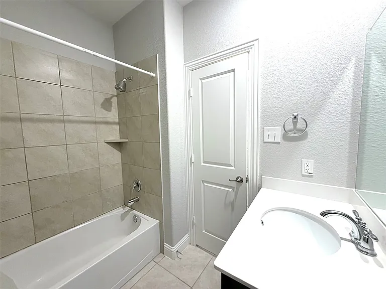 Bathroom featuring a white bathtub, light-toned tile surround with built-in shelf, chrome fixtures, and a white vanity with integrated sink and chrome faucet