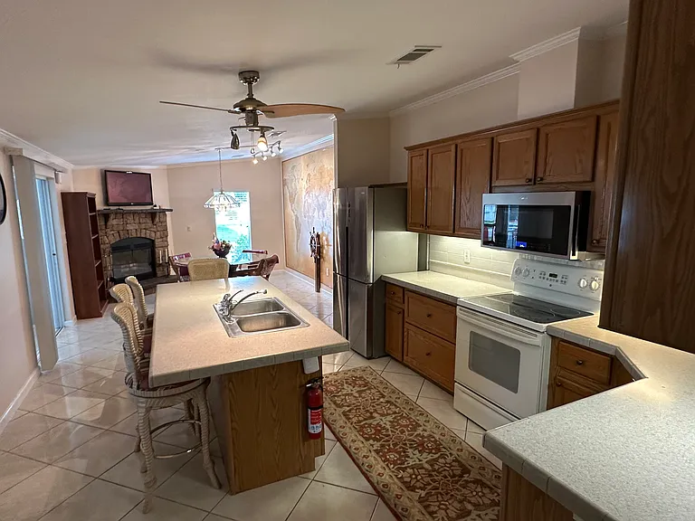 Large kitchen with 4-seated large bar setting with oak cabinets and view of kitchenette and fireplace.