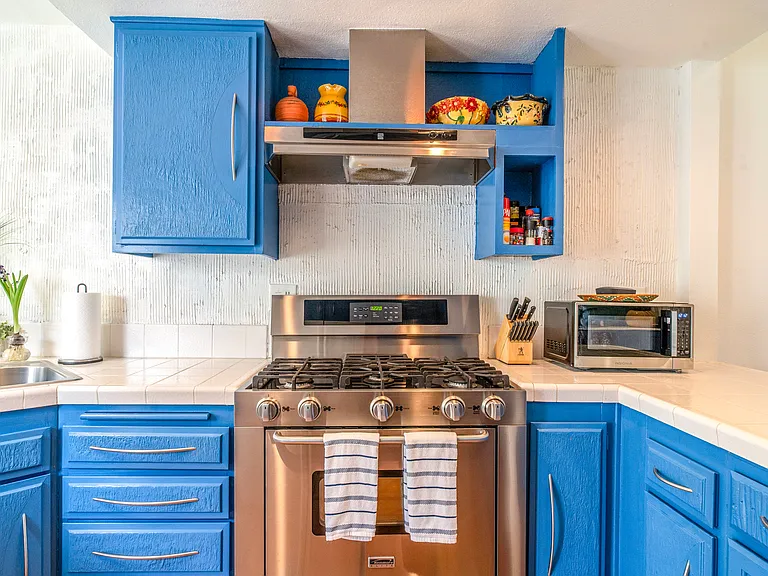 Bright, fully equipped kitchen with upgraded stainless gas range, custom blue cabinetry, tile countertops, and built-in storage. Designed for extended stays with quality cookware and thoughtful details throughout.