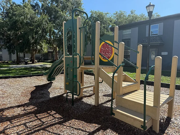 Inviting playground with a slide and climbing structure surrounded by lush greenery, perfect for family fun in a tranquil apartment community.