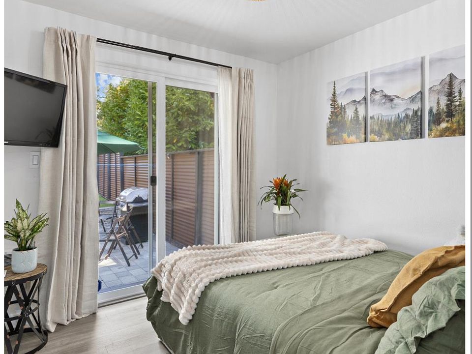 Bright room with backyard access and fresh breeze through the screen door. Features a 40" Smart TV, spacious closet, two sets of towels, live plants, wall art, and a foldable desk/workstation for comfort and convenience.