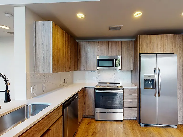 Apartment kitchen with stainless steel appliances, quartz countertops and wood-style flooring.