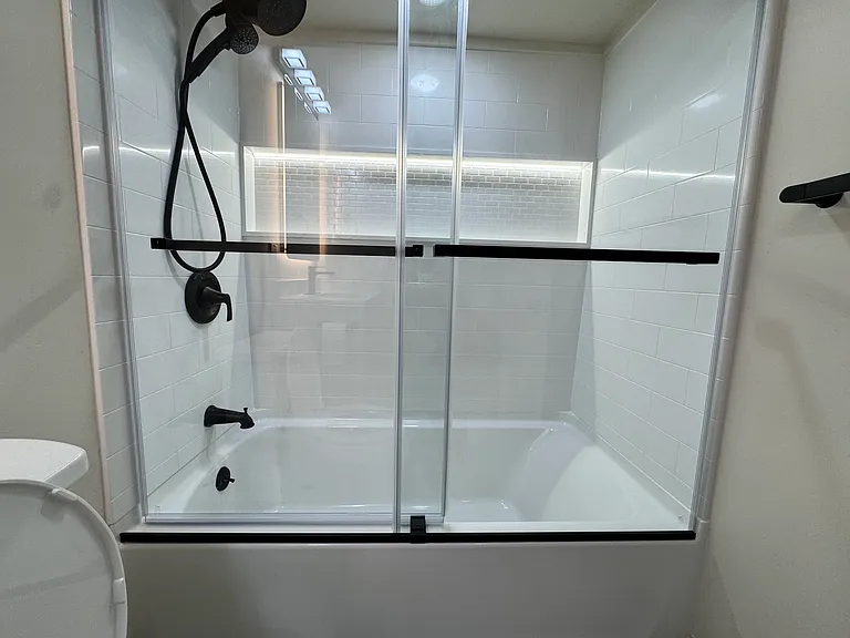 New bathroom featuring a modern vanity, LED-lit anti-fog mirror, and a tub/shower combo with sliding glass doors.