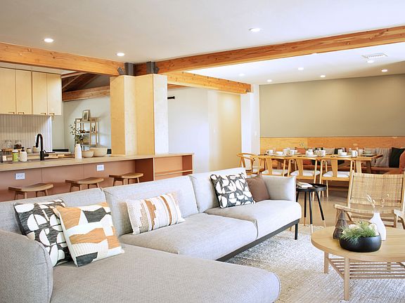 Open living, dining, and kitchen with exposed wood beams and ample seating.