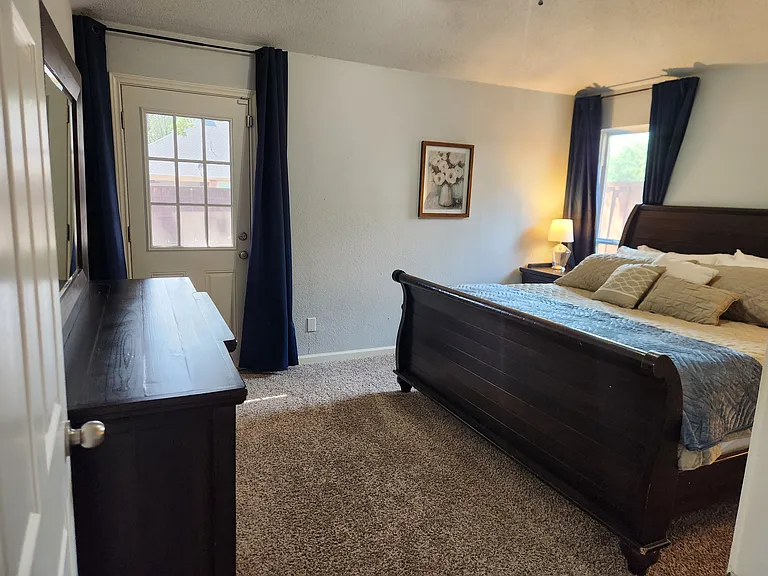 Primary suite features King bed, dresser, nightstands, mirror, TV and en suite bathroom w/ walk in closet. Private door to back patio and window.