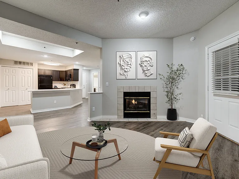 Modern open-concept living room with cozy fireplace, stylish artwork, and a spacious kitchen featuring dark cabinetry and sleek countertops.