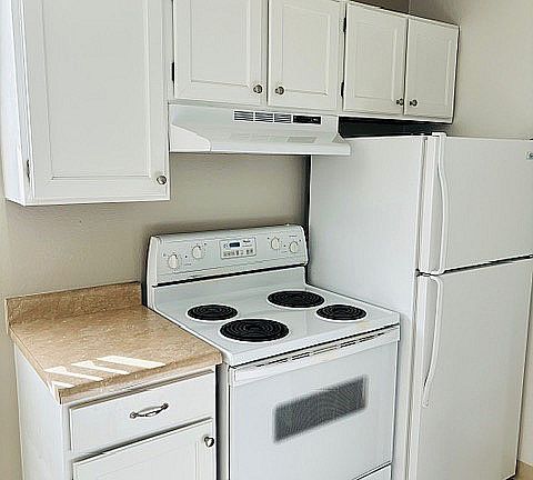 Bright, compact kitchen with white cabinetry, electric stove, and fridge, perfect for modern living.