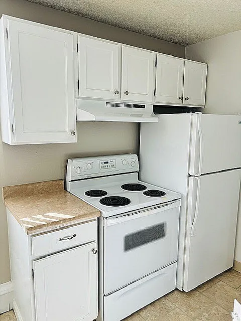 Bright, compact kitchen with white cabinetry, electric stove, and fridge, perfect for modern living.
