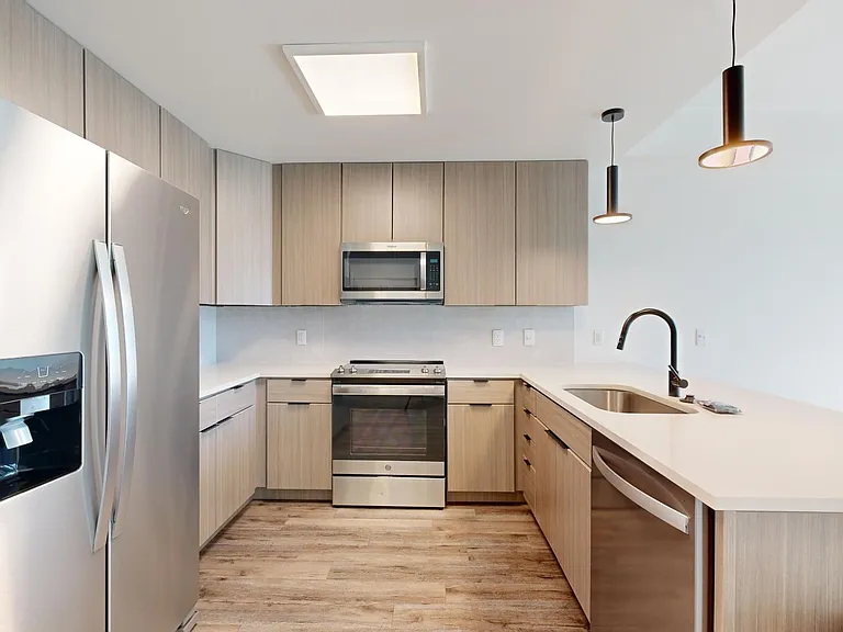Apartment kitchen with stainless steel appliances, quartz countertops, and wood-style flooring.