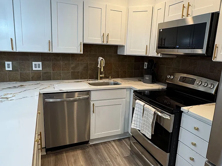 Efficient L-shaped kitchen with ample shaker cabinetry, stone-look counters, tile backsplash, and stainless appliances.