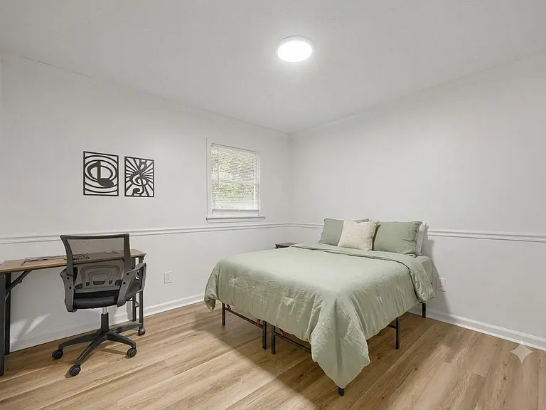 Furnished bedroom with a full bed, dedicated desk and chair, and a window for natural light over durable wood-look flooring.