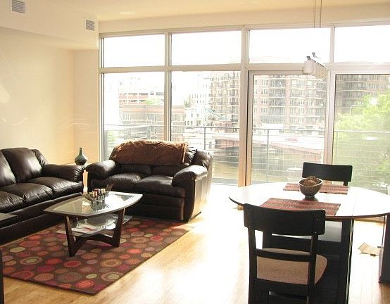 Living room with a wall of windows including East and North views of the river and city.
