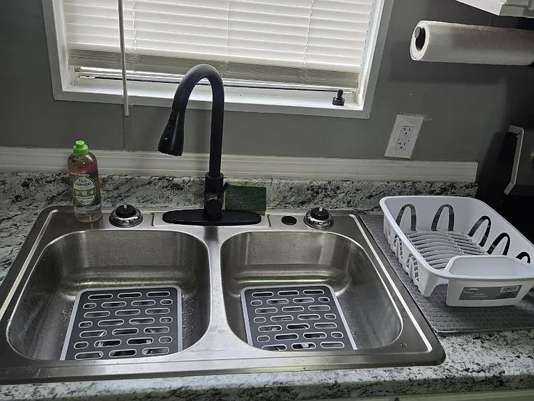 Kitchen sink area with a double-basin stainless sink, gooseneck faucet, and granite-look counters beneath a window.