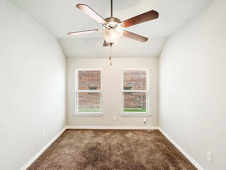 Room featuring a vaulted ceiling with a ceiling fan, two windows with blinds, brown carpet, and white baseboards