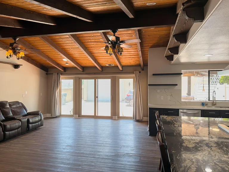 Open-concept living area with exposed beam ceilings, ceiling fans, and sliding doors opening to the patio.