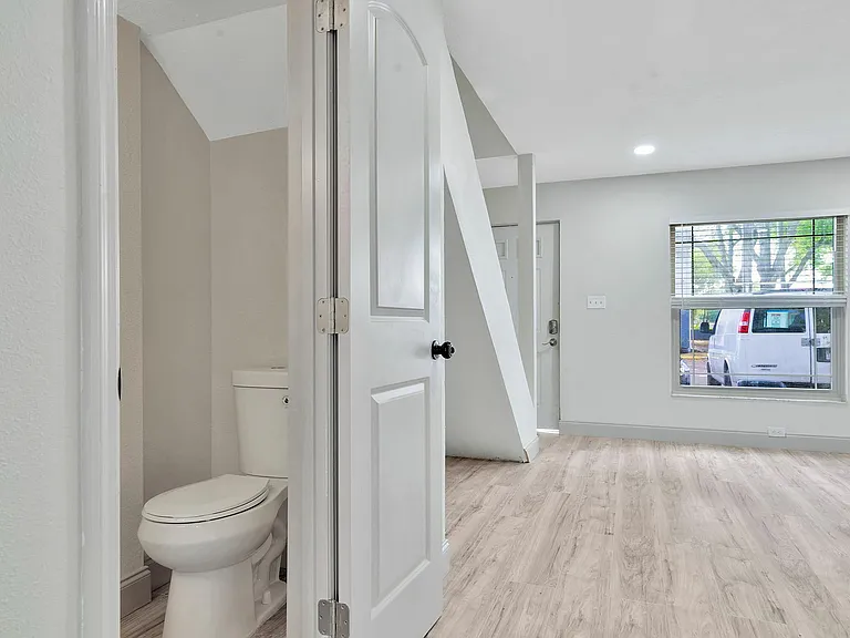 Modern apartment interior featuring sleek hardwood flooring, fresh white paint, and a bright, inviting space with a convenient half-bathroom.