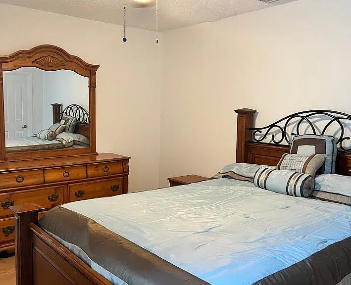 Furnished bedroom featuring a queen bed set, matching dresser with mirror, and a ceiling fan with light for comfort.