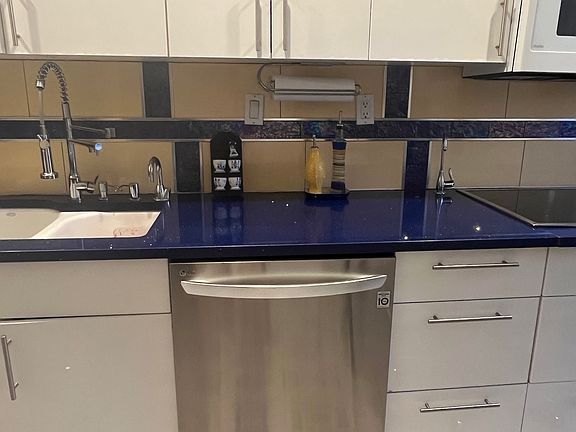 Modern kitchen with cobalt-blue quartz counters, stainless-steel dishwasher, and custom white cabinetry. Designer tile backsplash and patterned floor add elegance, while a deep-basin sink and pull-down faucet make cooking effortless.