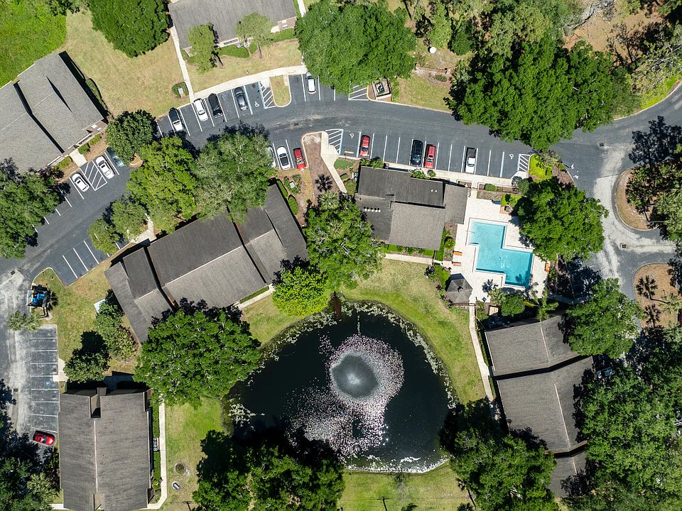 Drone view of The Park at Countryside Apartments showing pond with fountain, resort-style pool, surrounding buildings, parking areas, and mature trees.