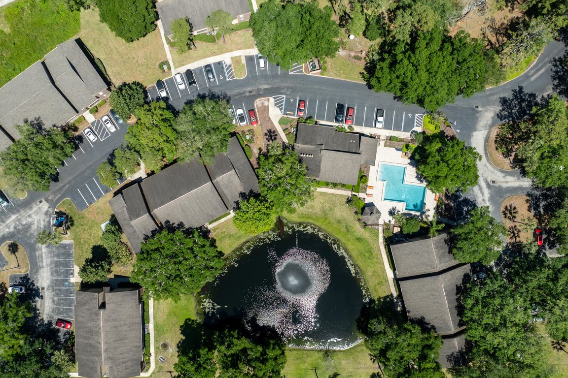 Drone view of The Park at Countryside Apartments showing pond with fountain, resort-style pool, surrounding buildings, parking areas, and mature trees.
