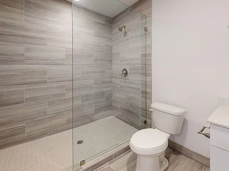Modern bathroom featuring a sleek glass-enclosed shower, beige tiled walls, and a pristine vanity.