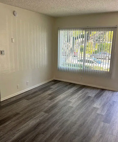 Front room with large window and wood plank style flooring in unit at Los Robles Apartments in Pasadena, California.